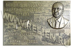 Мемориальная памятная доска с фоновым рисунком в виде глубокой гравюры, посвященная М.С. Рудяку. Размер 80 х 120 х 4 (торец) см. Мемориальная памятная доска (плита) изготовлена по заказу благотворительного фонда памяти Михаила Рудяка. При изготовлении модели мемориальной памятной доски применена технология гравюры глубокой печати и литья выпуклых букв. При моделировании мемориальной доски применялись приёмы ручной лепки портрета и других объёмных деталей по фотографиям и эскизам. При снятии литьевой формы использовались высокотехнологичные эластичные формовые материалы. Окончательное изготовление мемориальной памятной доски (плиты) произведено по технологии холодного литья "порошковой бронзой" (порошка бронзы и долговечного атмосферостойкого полимерного связующего) в форму с армированием стальными прутами и уголками. Мемориальные памятные доски (плиты), изготовленные по этой технологии, имеют ряд преимуществ перед бронзовыми мемориальными досками.